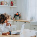 Lady with perfect dark skin holding credit card and inserting bank information for online shopping sits near laptop closeup